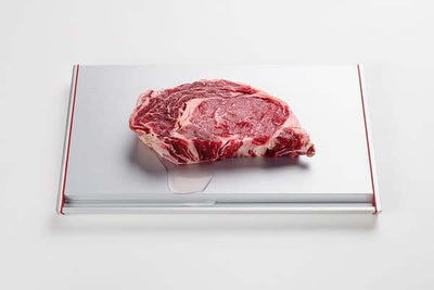 Modern defrosting tray with raw steak, showing heat fins and drip channel for quick, natural thawing.