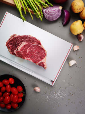 Steak defrosting on ThawTHAT! Modern Defrosting Tray surrounded by fresh vegetables in a kitchen setting.