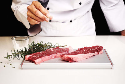 Chef using ThawTHAT! Modern defrosting tray with steaks, showcasing efficient and natural thawing with contemporary design.